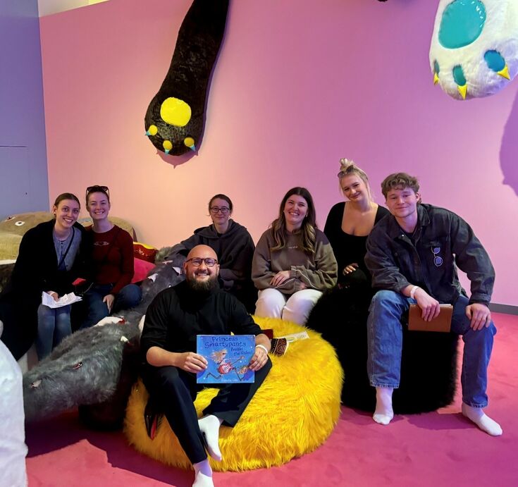 Gruppenfoto Studierende mit Dozent sitzend auf einer Ausstellung