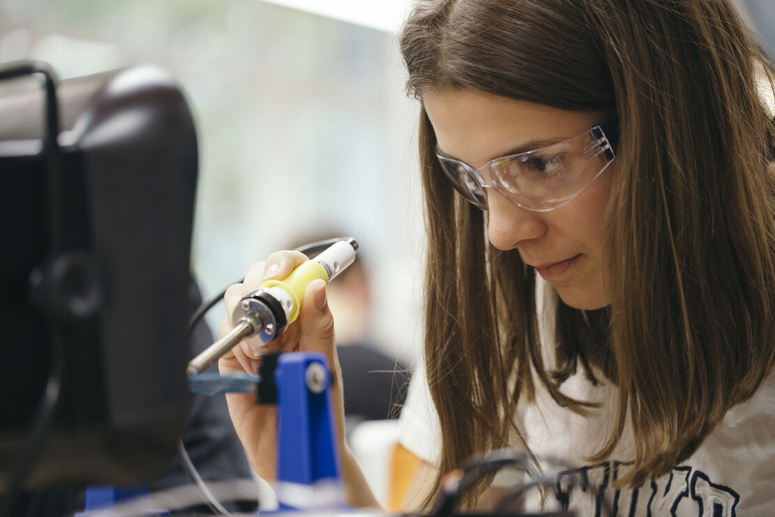 Schülerin mit Schutzbrille und Lötkolben