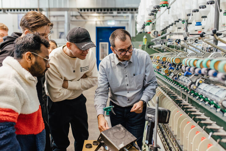 Professor erklärt Studierenden Spinnmaschine in Maschinenhalle