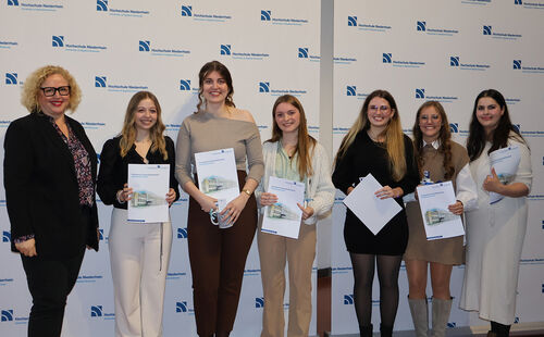 sechs Absolvierende bei einer Abschlussfeier mit einer Dozentin