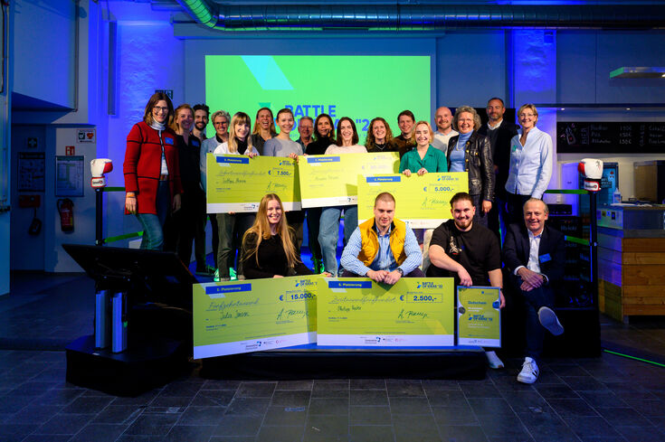 Gruppenfoto der Gewinner, der Jury und den Organisatoren der Veranstaltung. Alle freuen sich. Die Gewinner halten ihren übergroßen Check in der Hand.