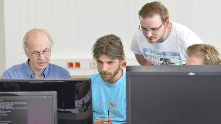 Four men look at a monitor